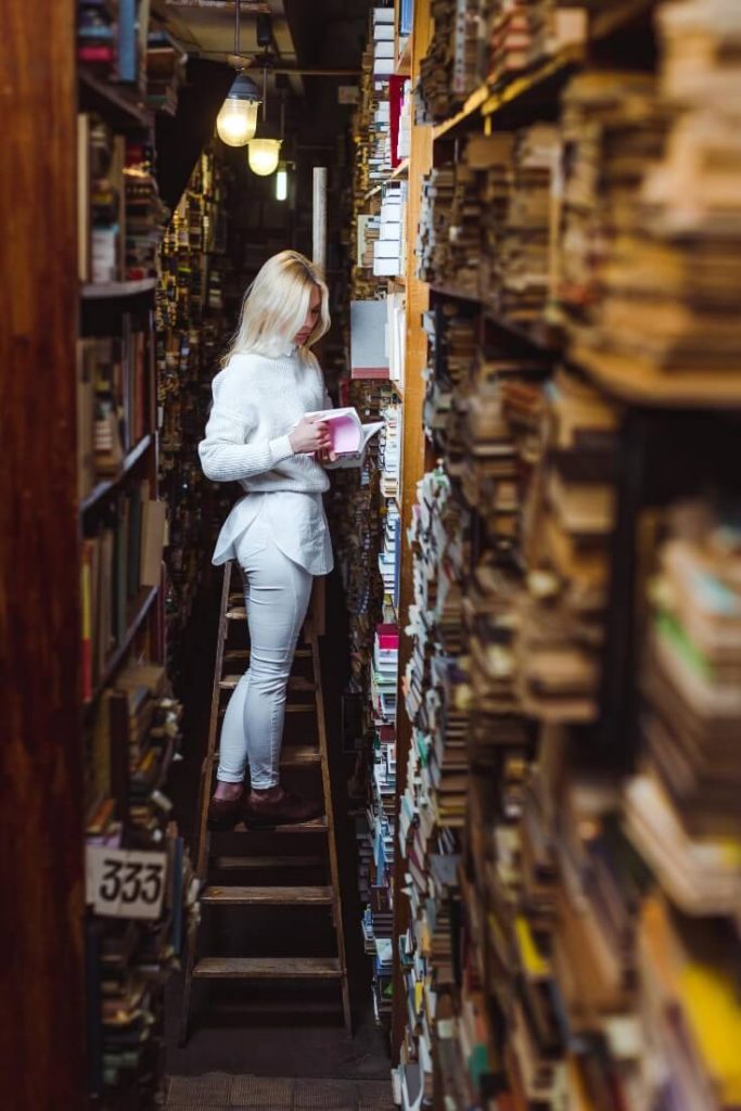 Lady climbing a ladder to reach books in a library