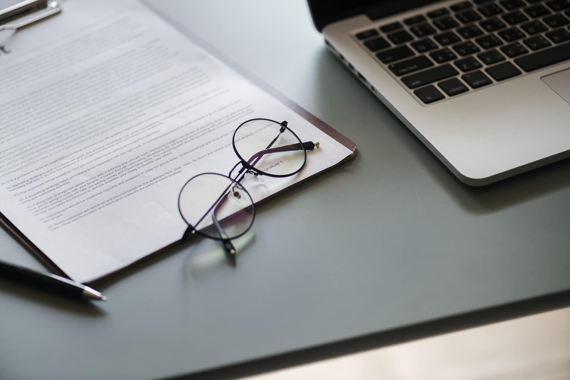 CV lying on a desk with a pair of glasses on top and a laptop close by