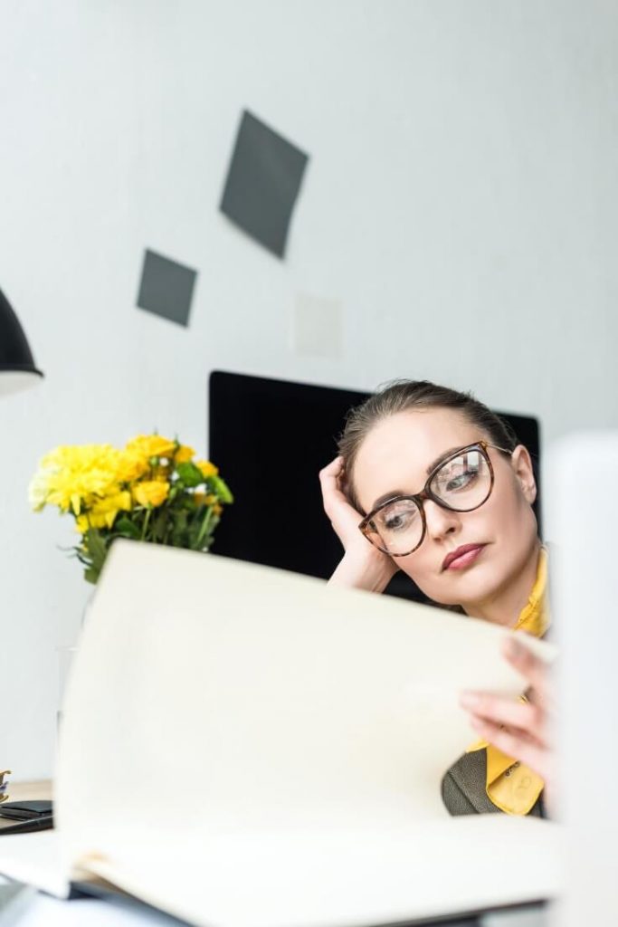 A lady looking bored  whilst reading a document at her desk