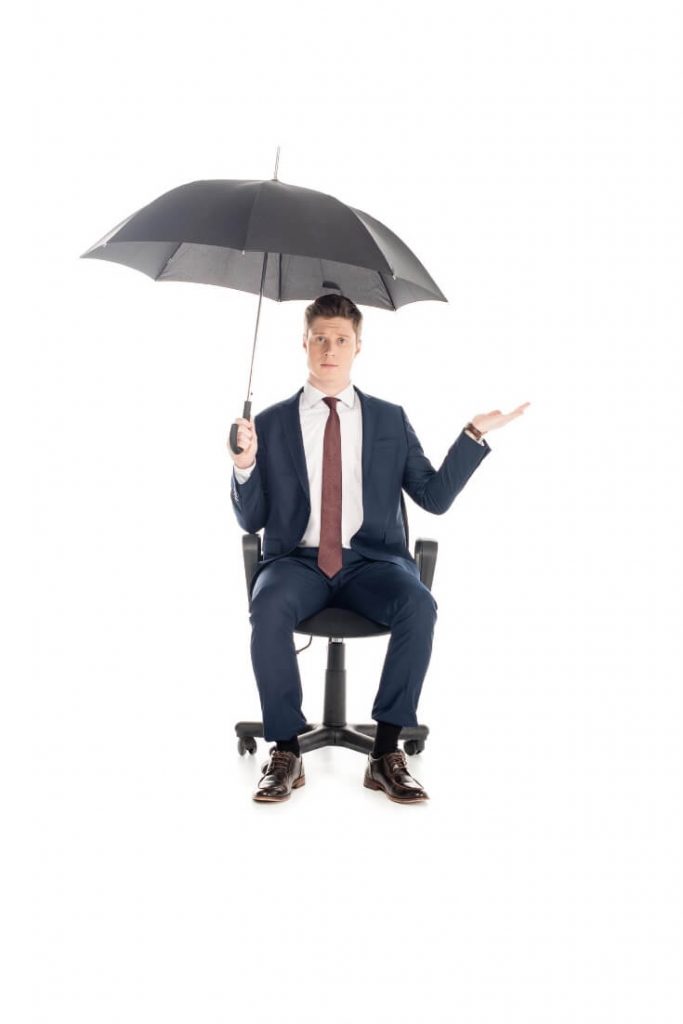 A man in a business suit sitting on an office chair holding an umbrella - will this rain stop Adria? No it won't!