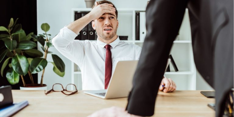 a man has removed his glasses and looks worried while working on his computer