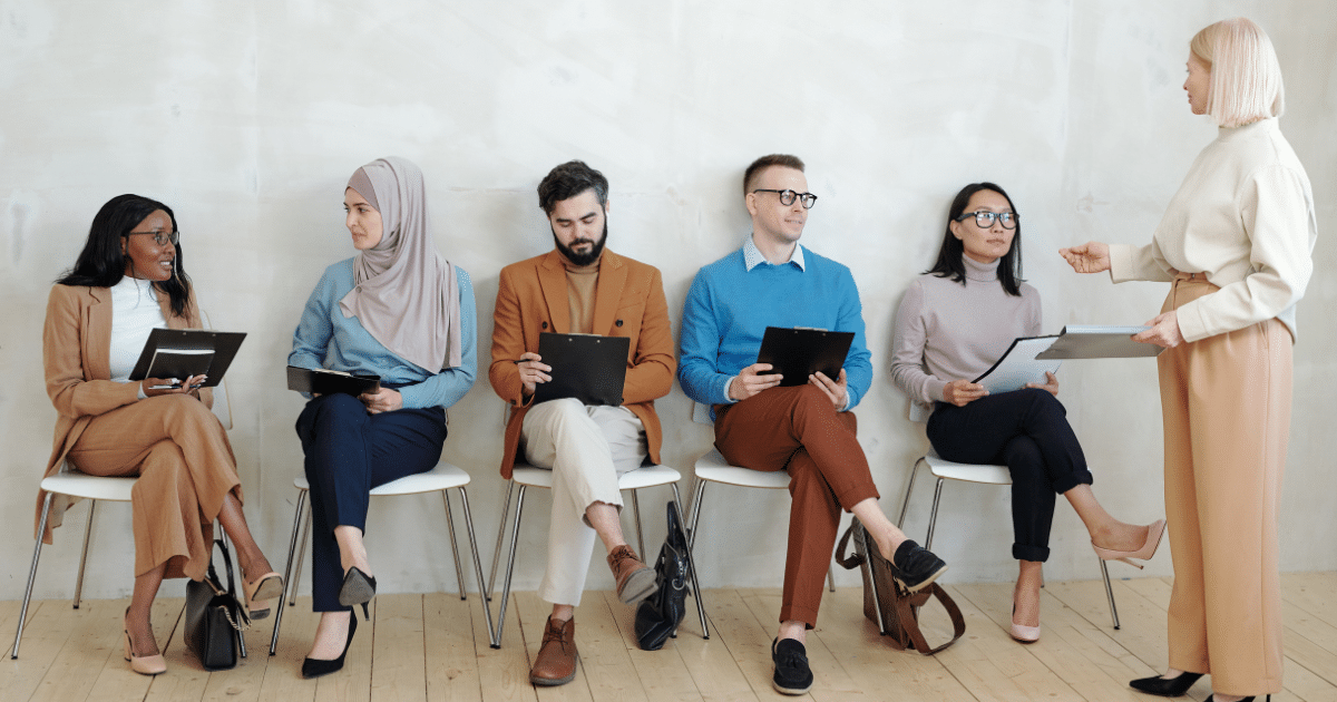 three woman and two men from diverse ethnicities wait their turn to be interviewed by an older women