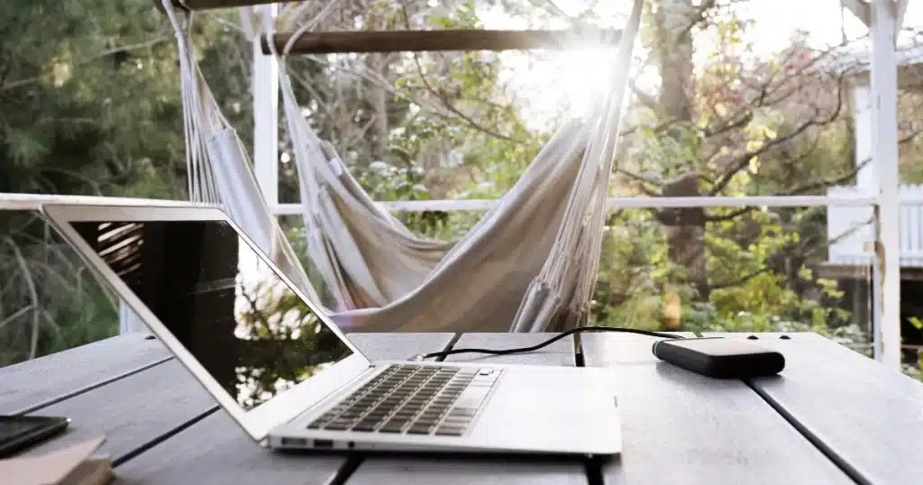 An empty work desk of a digital nomad in an exotic holiday destination. On the background, an hammock.