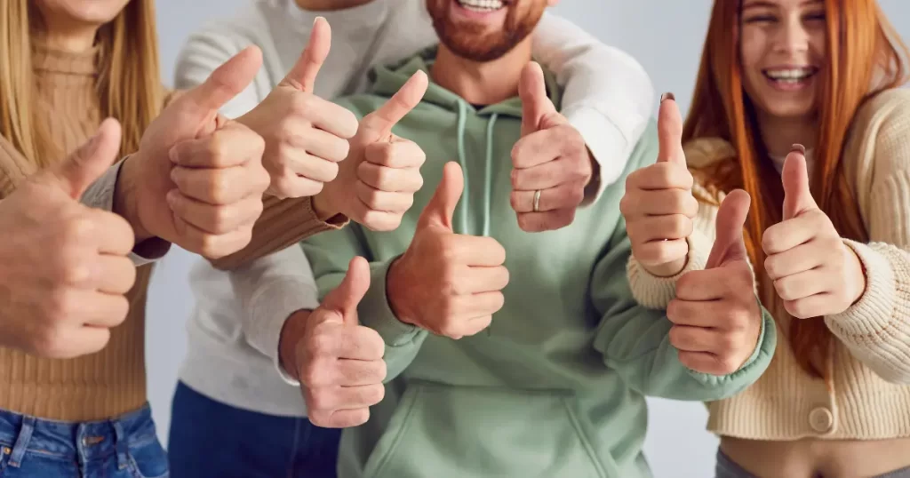 Two women and two mean smile and show their approval with their thumbs up