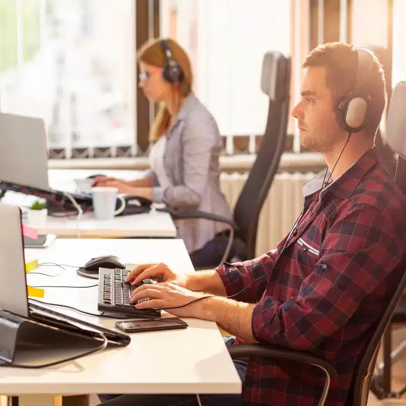 A men and a woman working in tech in their office while listening to music on their headphones