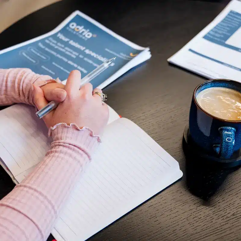 Woman takes notes in a meeting with a member of the Adria Solutions team