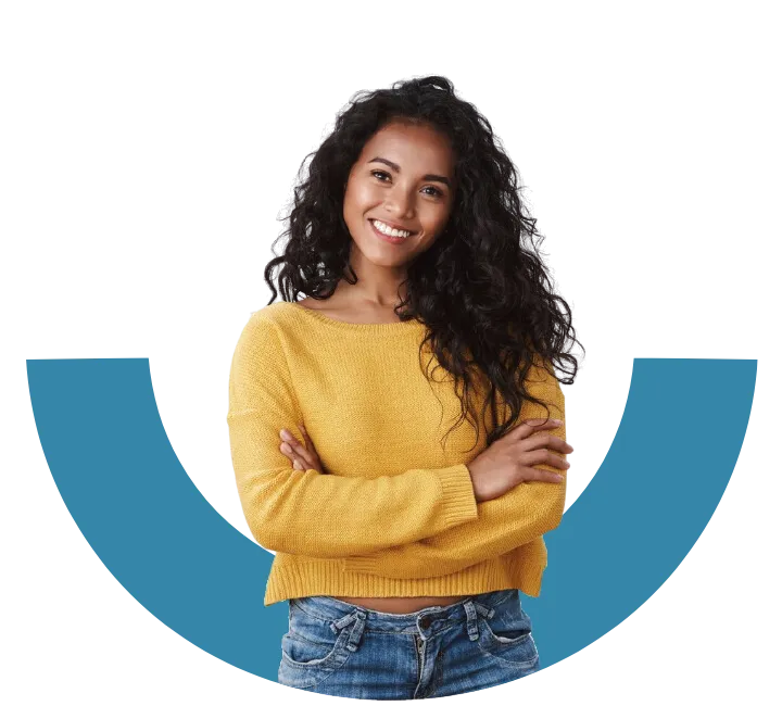 A young black woman with a yellow jumper and jeans crosses her arms and smiles confident