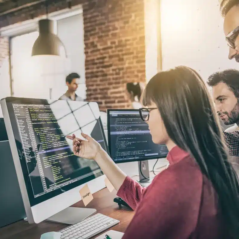 a woman points at a bug in the code watched by two colleagues