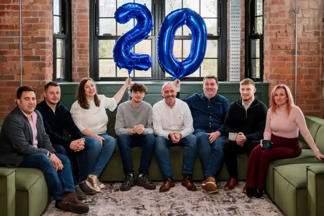 The team of Adria Solutions celebrates 20 years in business with a big balloon reading "20"