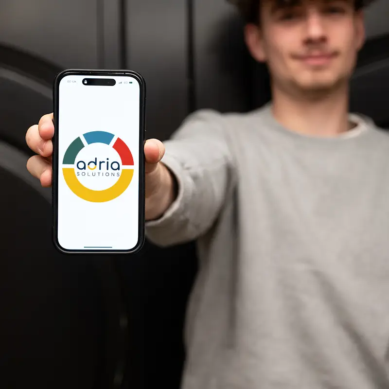 A young man holds a phone with Adria Solutions' logo on it