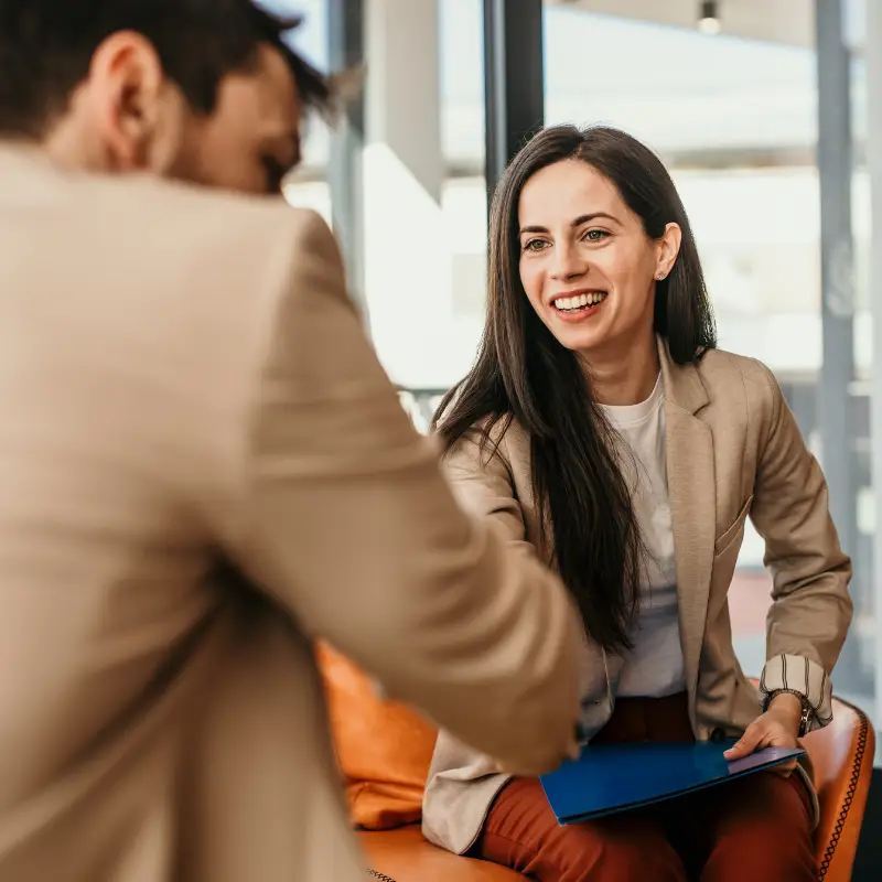 A male hiring manager welcomes a woman, his company's new hire, into his hybrid office